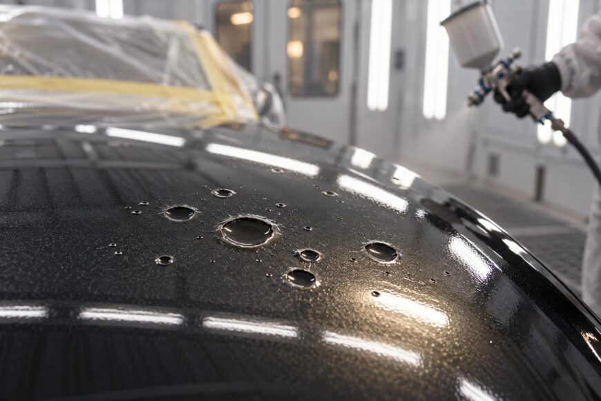 Close-up of fisheye defects and craters on a freshly painted black car hood in a spray booth
