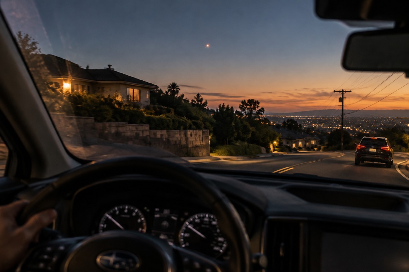 Interior view from a Subaru Crosstrek driving down a suburban street at dusk with a mysterious glowing UFO in the evening sky