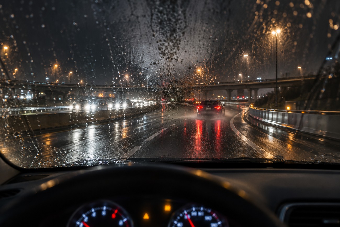 Driver POV from inside a Kia Forte looking at a wet highway with oncoming headlights at night during rain
