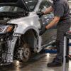 Mechanic wearing black gloves aligns a new replacement fender on the side of a car in a repair shop