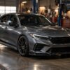 A grey sports sedan with a custom aerodynamic body kit parked inside a professional garage workshop