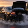 A black Dodge Charger with its trunk open containing a fog machine emitting dense smoke onto the ground