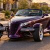 A purple Plymouth Prowler factory hot rod parked on a sunny suburban street with exposed front wheels
